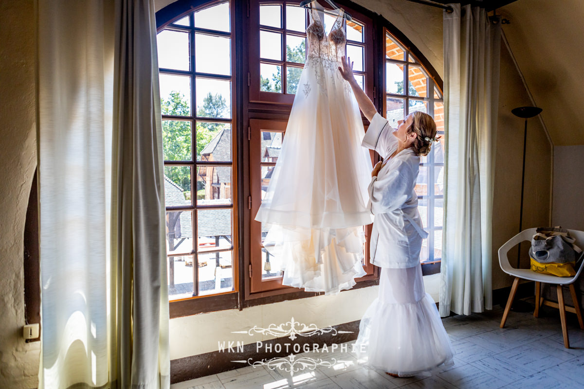 Claire s'apprête à enfiler sa robe de mariée, un moment émouvant capturé aux Écuries de Rivaulde.
